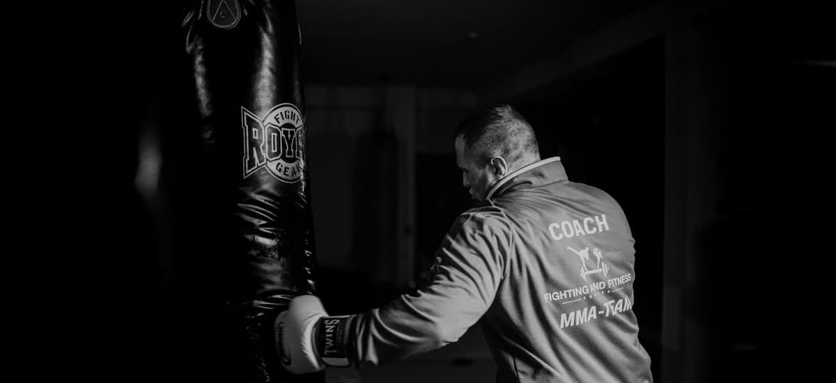 A boxing coach practicing punches on a heavy bag indoors, showcasing strength and focus.