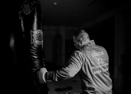 A boxing coach practicing punches on a heavy bag indoors, showcasing strength and focus.